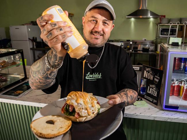 Lowrider Cafe owner Matthew Hill with a 'Lowrider breaky bagel' at his Morphett Vale cafe and barber shop, on May 20th, 2024.Picture: Tom Huntley