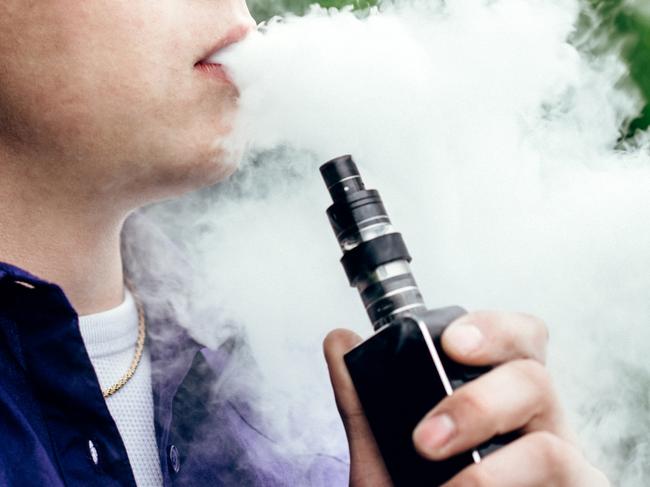 A young adult male has a cloud of nicotine vapor "smoke" pouring from his mouth.  Vape smoking, or "vaping" is growing in popularity, as well as falling under stricter state and governmental regulations.  Horizontal image with copy space.