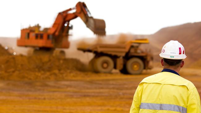 A mine worker watches as a haul truck is loaded by a digger with material from the pit at Rio Tinto Group's West Angelas iron ore mine in Pilbara, Australia, on Sunday, Feb. 19, 2012. Rio Tinto Group, the world's second-biggest iron ore exporter, will spend $518 million on the first driverless long-distance trains to haul the commodity from its Western Australia mines to ports, boosting efficiency. Photographer: Ian Waldie/Bloomberg