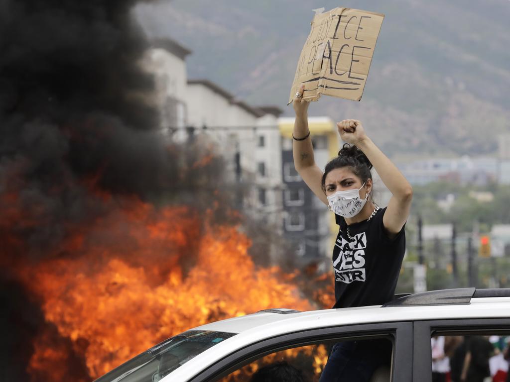 A protester looks on as a flipped over police vehicle burns in Salt Lake City. Picture: Rick Bowmer/AP