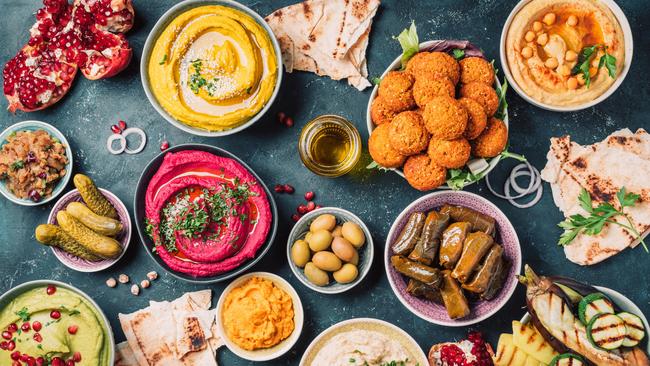 Middle Eastern meze with pita, olives, colorful hummus, falafel, stuffed dolma, babaganush, pickles, vegetables, pomegranate, eggplants.