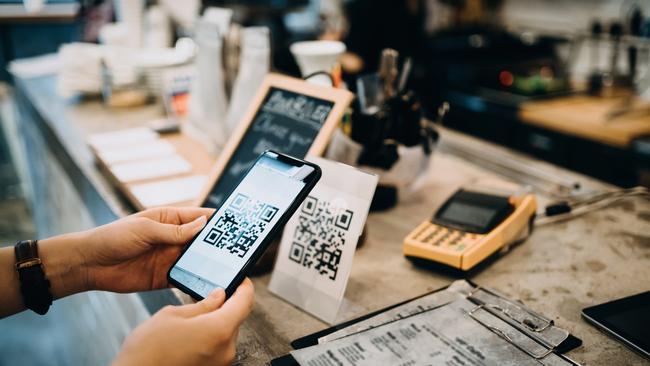 Customer scanning QR code, making a contactless payment with her smartphone in a cafe