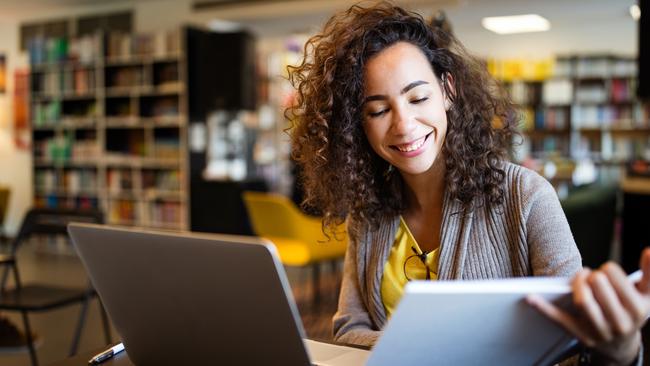 Young afro american woman sitting at table with books and laptop for finding information. Young student taking notes from laptop and books for her study in library.