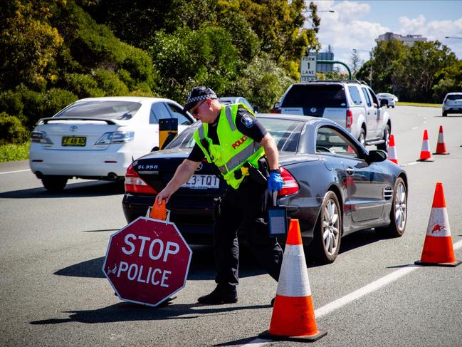 A Queensland police officer moves a stop sign at a vehicle checkpoint on the Pacific Highway on the Queensland - New South Wales border, in Brisbane on April 15, 2020. - A state border that bisects Australia's neighbouring beachside towns of Coolangatta and Tweed Heads has rarely troubled locals, long accustomed to crossing the invisible line daily for coffee or a surf. But as Australia began shutting down last month in response to the coronavirus outbreak, Queensland closed its border to slow the virus spread from worst-hit New South Wales (NSW) state -- for the first time since the Spanish Flu pandemic a century ago. (Photo by Patrick HAMILTON / AFP)