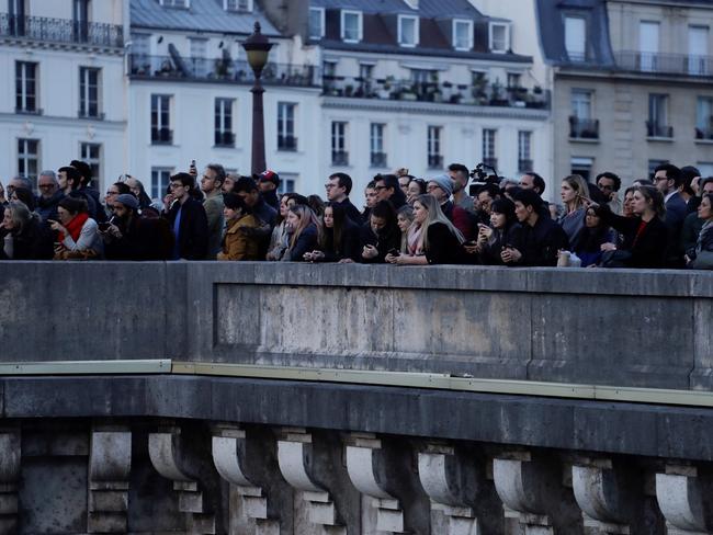 People stand on a bridge looking at smoke and flames rising during a fire at the landmark Notre-Dame Cathedral in central Paris on April 15, 2019. (Photo by Thomas SAMSON / AFP)