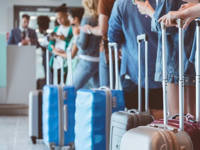 Travelers with luggage using smart phones while waiting in line for boarding at airport. Focus on wheeled luggage.