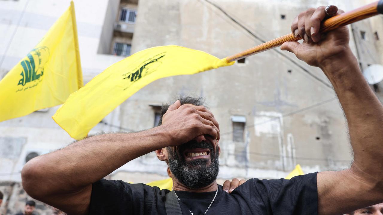 A man reacts while holding a Hezbollah flag during the funeral of people killed after Tuesday’s attacks. (Photo by ANWAR AMRO / AFP)