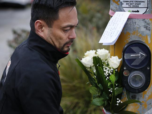 Louis Datoi tapping a flower tribute to the pedestrian light pole. Picture: David Caird