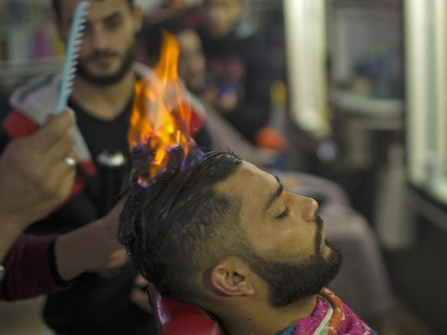 A client’s hair is set on fire by Mr Edwan. Picture: Mahmud Hams/AFP