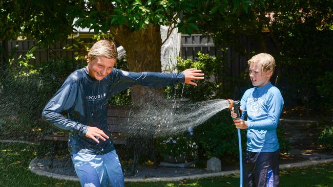 Lachlan Fettke 13, and his brother Jacob, 10, from Marion try to keep cool in the traditional Australian way with a sprinkler in the backyard. Picture: Brenton Edwards