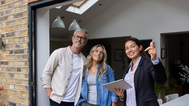 Real estate agent showing a house for sale to a couple and pointing outside - home ownership concepts