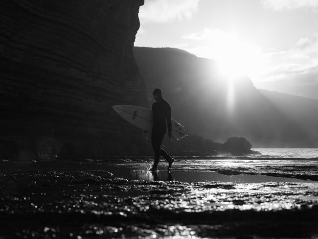 Surfer Marti Paradisis walking along the back ledge at Shipstern Bluff before paddling out as the sun rises in the background. Picture: Matt Dunbar