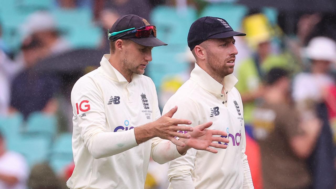 England's captain Joe Root (L) talks with team mate Jack Leach as they walk off the ground as rain falls on day two of the fourth Ashes cricket Test between Australia and England at the Sydney Cricket Ground (SCG) on January 6, 2022. (Photo by DAVID GRAY / AFP)