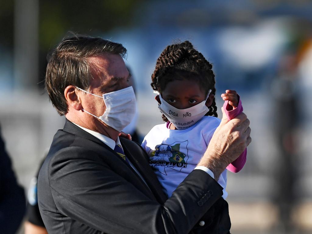 Anti-vaccine Brazilian President Jair Bolsonaro holds a girl, both wearing face masks, during the flag-raising ceremony. Picture: AFP