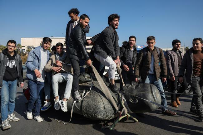 Damascus University students stand on a toppled statue of Syria's late president Hafez al-Assad during a rally near the campus