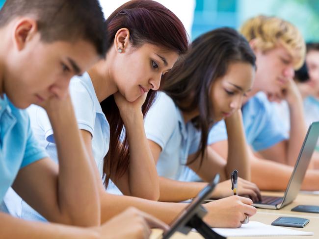 Row of private high school students work on assignment in class. They are writing or using laptops or digital tablets. They are concentrating as they study. They are wearing school uniforms.