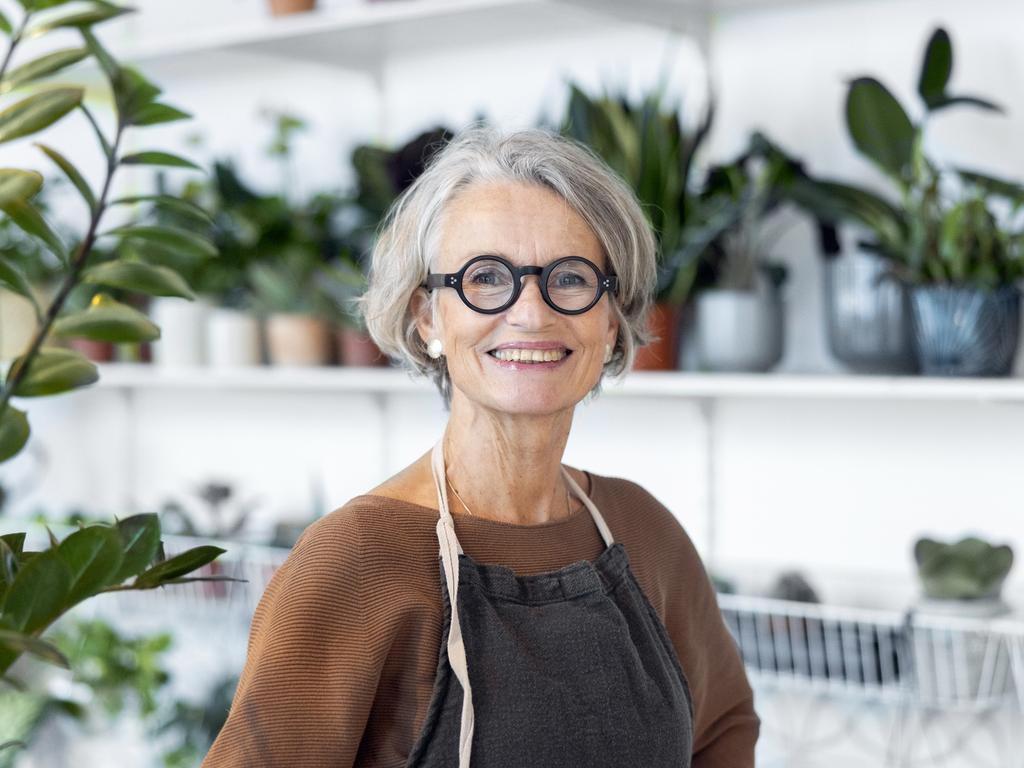 Portrait of senior female florist at small business flower shop. Happy mature woman wearing apron working in a small flower store; working in retirement happy retiree worker generic