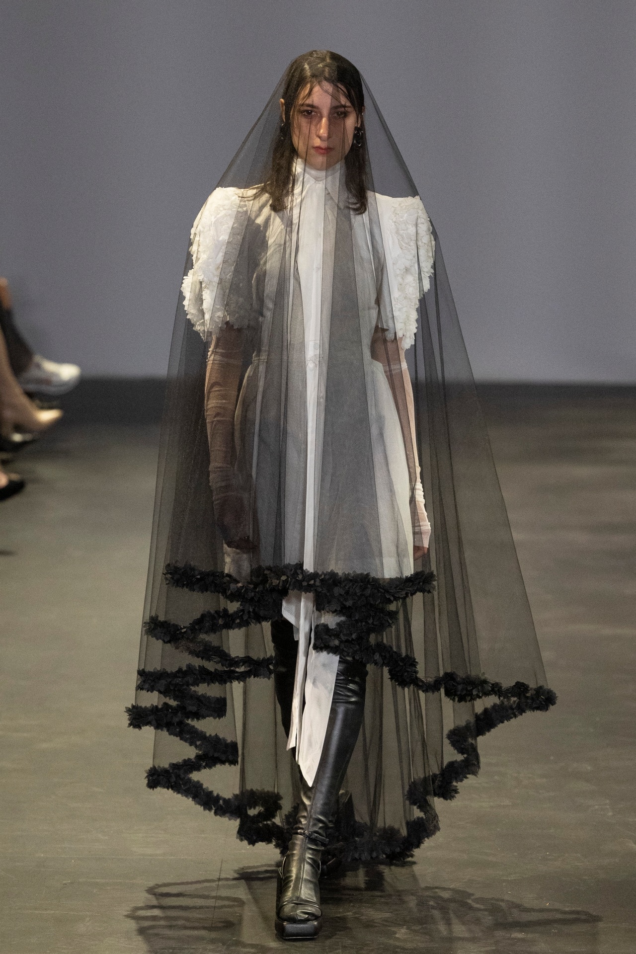 <p><em>Gail Sorronda. Image credit: Getty</em></p><p>But this year, there was a darker undercurrent in the air. And it felt like the right step outside of the box of expectations. At Gail Sorronda, the Brisbane-native's presentation embraced the feminine and the macabre at once. Models walked in pouffed and frilled frocks, ivory-white and primly buttoned. But these weren't your average period drama heroines: skin-tight latex boots grounded the looks, adding a punkish edge to the romantic blouses and dresses. Shrouded in black veils, they were like glum, fashionable mourners. </p>