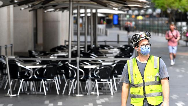 A worker with a face mask walks next to a closed restaurant at Sydney’s Circular Quay. Picture: AFP