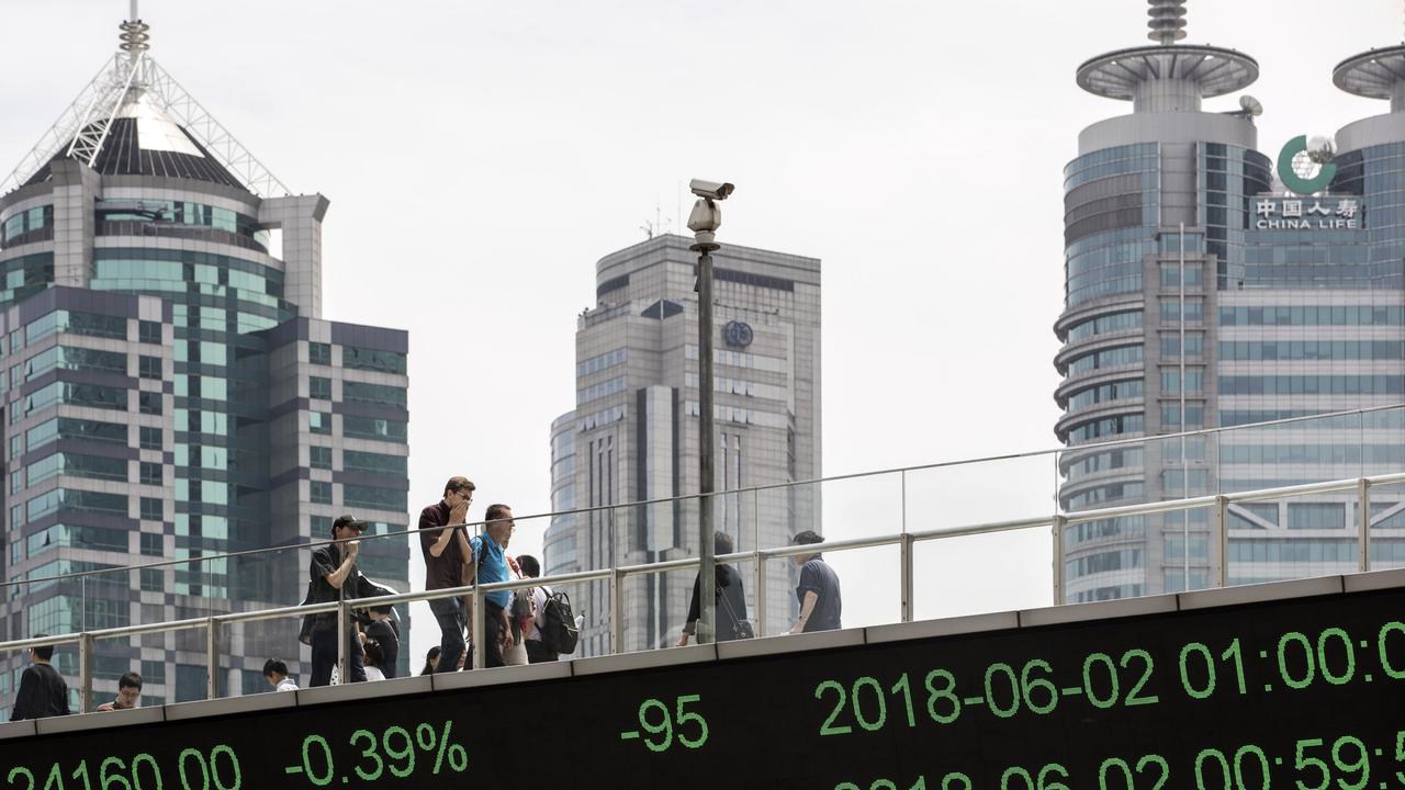 People walk along an elevated walkway as an electronic ticker displays stock figures in Pudong's Lujiazui Financial District in Shanghai, China