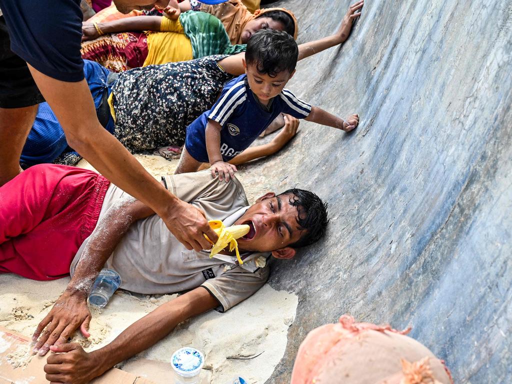 A man gives a banana to a newly-arrived Rohingya refugee resting on a beach in Sabang Island, Indonesia. Picture: Chaideer Mahyuddin/AFP