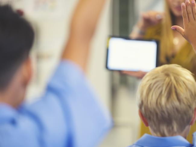 Elementary school  teacher giving a presentation to the class. The students have their hands raised to ask  questions in the classroom