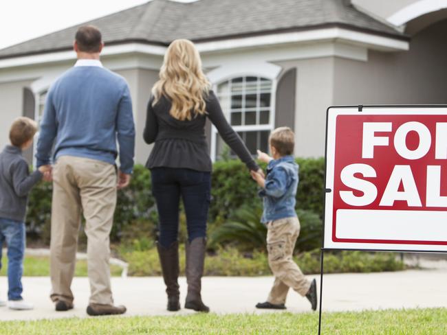 Family with two boys (4 and 6 years) standing in front of house with FOR SALE sign in front yard.  Focus on sign.