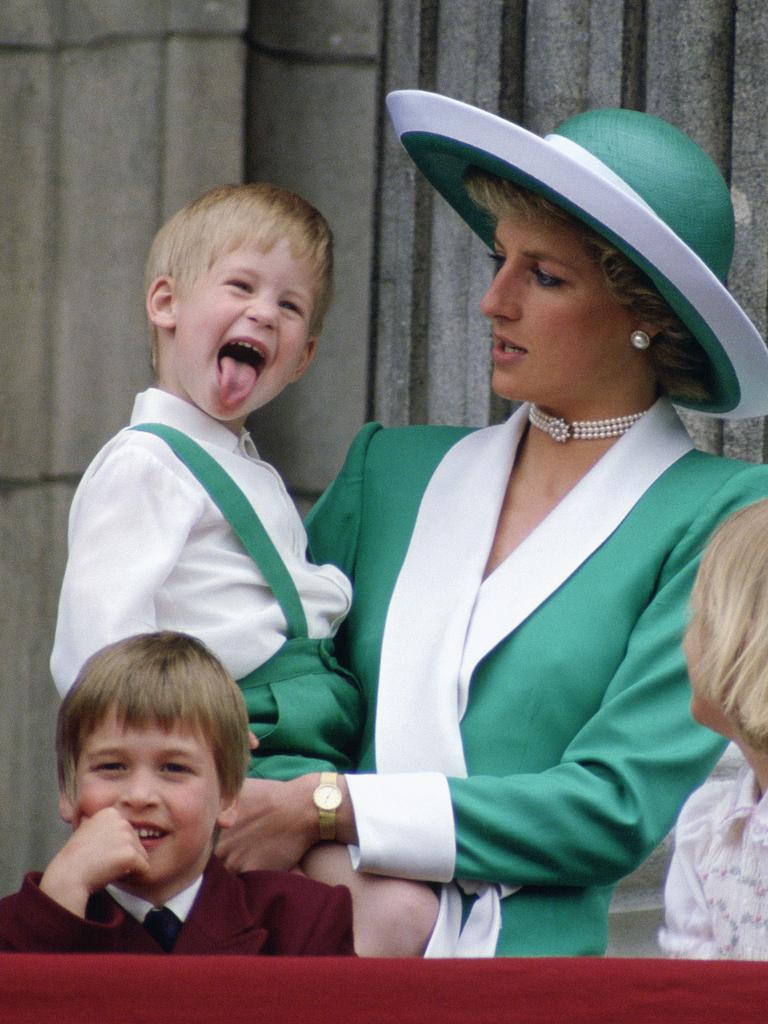 <b>1988:</b> The world gets its first real glimpse of Harry the extrovert as the cheeky royal, wearing a green outfit to match his mum Princess Diana, pokes his tongue out while watching Trooping the Colour as a bemused Prince William looks on. Picture: Tim Graham/Getty