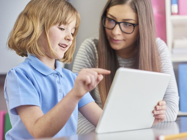 a young teacher listens as her young pupil explains what she is reading on a digital tablet . The little girl is excited as she explains to her teacher . Picture: Istock