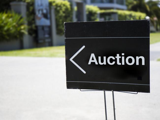 Auction sign, outside suburban home, positioned on front lawn.