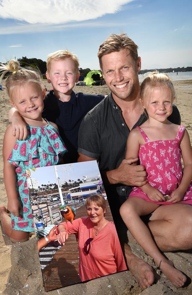 Sam Mitchell with his children, Smith, Emmy and Scarlett holding a photo of his mother-in-law, Valda. Picture: Tony Gough