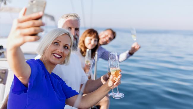 Smiling group of friends traveling on a yacht and drinking champagne. Mature adult friends sitting on sailboat's deck and drinking champagne enjoying the view