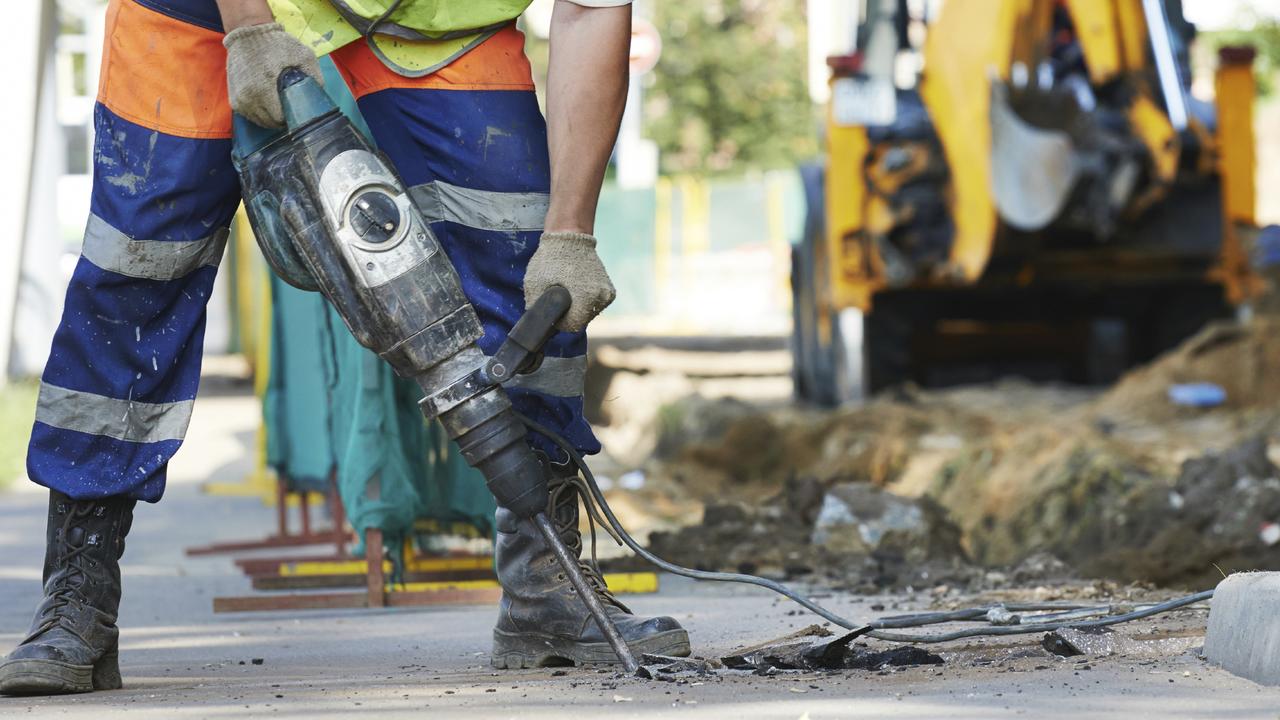 Builder worker with drill equipment breaking asphalt at road construction site