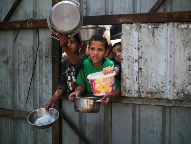 TOPSHOT - Palestinian children reach out with their pots as they wait for food at a distribution point in Nuseirat, central Gaza Strip, June 2, 2025. Israel has faced growing condemnation over the humanitarian crisis in the war-ravaged Gaza Strip, where the United Nations has warned the entire population faces the risk of famine after no aid was allowed to enter for more than two months. (Photo by Eyad BABA / AFP)