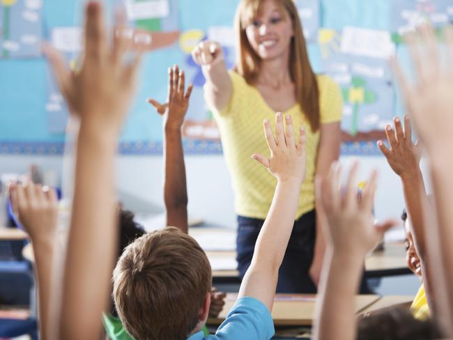 Mature woman (40s) teaching class of multi-ethnic elementary school children. Focus on boy in blue shirt.