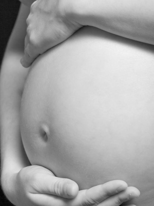 Black and white close-up of the belly of a pregnant woman who is gently supporting her unborn child