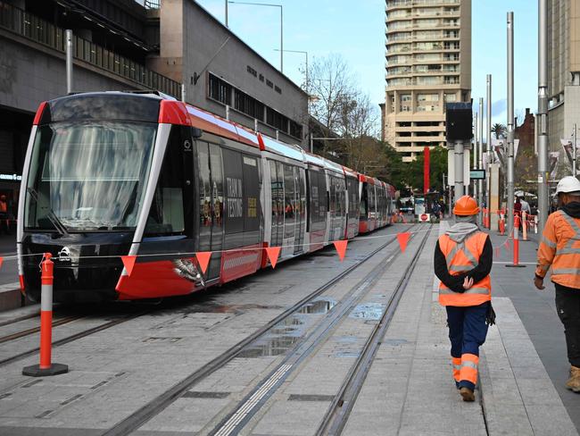 Construction workers walk past a tram parked at Circular Quay where the light railway tram reached the end of the 12.7 kilometre line for the first time in Sydney on July 30, 2019. - Cost blowouts, legal disputes, delays to construction and major disruption to businesses along the route have plagued Sydney's light railway project over the past three years, causing political upheaval for the state government. (Photo by PETER PARKS / AFP)