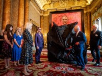 LONDON, ENGLAND - MAY 14: Queen Camilla, Artist Jonathan Yeo (5th L) and his family watch as King Charles III unveils his portrait by artist Jonathan Yeo in the blue drawing room at Buckingham Palace on May 14, 2024 in London, England. The portrait was commissioned in 2020 to celebrate the then Prince of Wales's 50 years as a member of The Drapers' Company in 2022. The artwork depicts the King wearing the uniform of the Welsh Guards, of which he was made Regimental Colonel in 1975. The canvas size - approximately 8.5 by 6.5 feet when framed - was carefully considered to fit within the architecture of Drapers' Hall and the context of the paintings it will eventually hang alongside. Jonathan Yeo had four sittings with the King, beginning when he was Prince of Wales in June 2021 at Highgrove, and later at Clarence House. The last sitting took place in November 2023 at Clarence House. Yeo also worked from drawings and photographs he took, allowing him to work on the portrait in his London studio between sittings. (Photo by Aaron Chown-WPA Pool/Getty Images)
