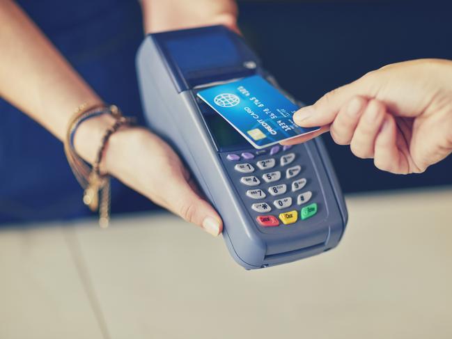 Close-up of customer making contactless payment through credit card. Female cafe owner is holding card reader at checkout counter. They are in coffee shop.