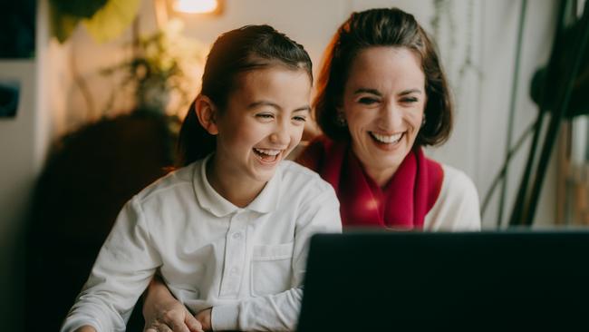 Young girl and her mother watching streaming video on laptop at home