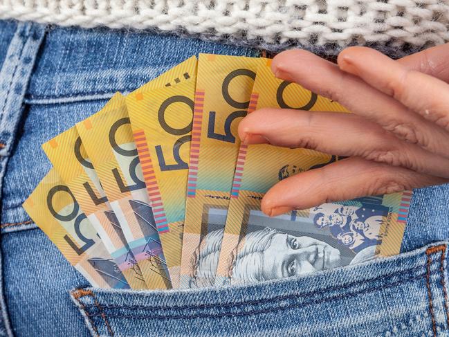 Female hand reaching for 50 Australian dollar bills in her jeans back pocket