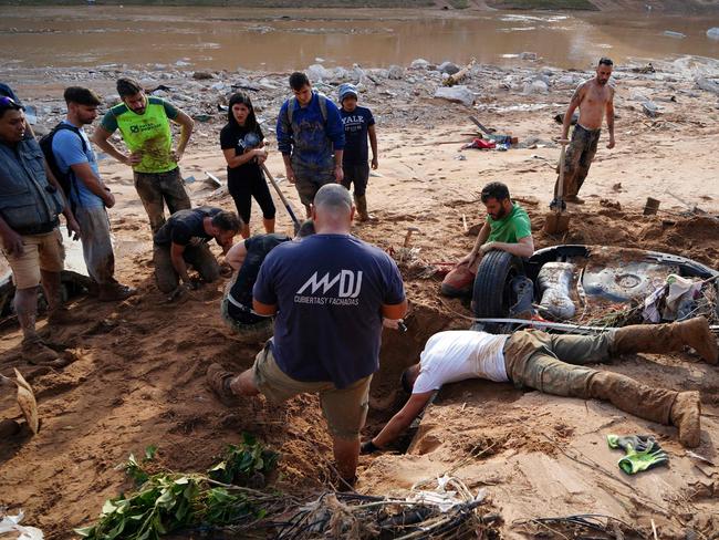 A group of people try to dig up a car in search of victims buried on the riverbank. Picture: AFP