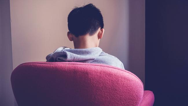 Sad preteen tween mixed Asian boy sitting alone in a big chair facing wall, depressed, autism awareness, children mental health concept