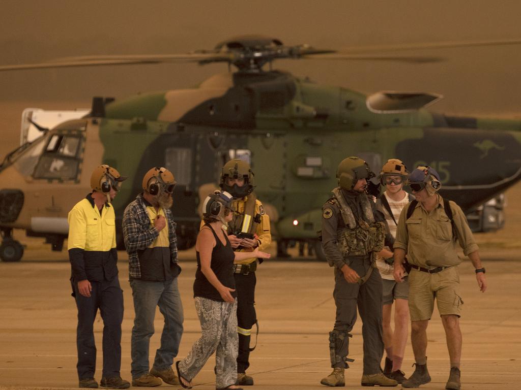 Members of the Tytherleign family are escorted from the HMAS Albatross 808 Squadron Flight line by Leading Seaman Aircrewman Ben Nixon and Rural Fire Service employee Dwyane Graham after being evacuated from their property near the Tianjara bushfire. Picture: ADF