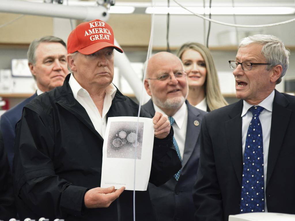 President Donald Trump holds a photograph of coronavirus as Dr Steve Monroe speaks at the headquarters of the Centers for Disease Control and Prevention in Atlanta on Friday. Picture: Hyosub Shin/Atlanta Journal-Constitution via AP