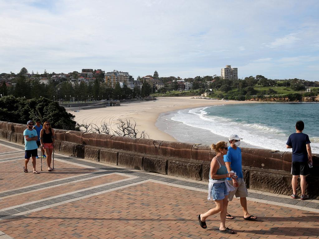 People walk along the beach front of a closed Coogee beach, 29th March 2020. Picture: Damian Shaw