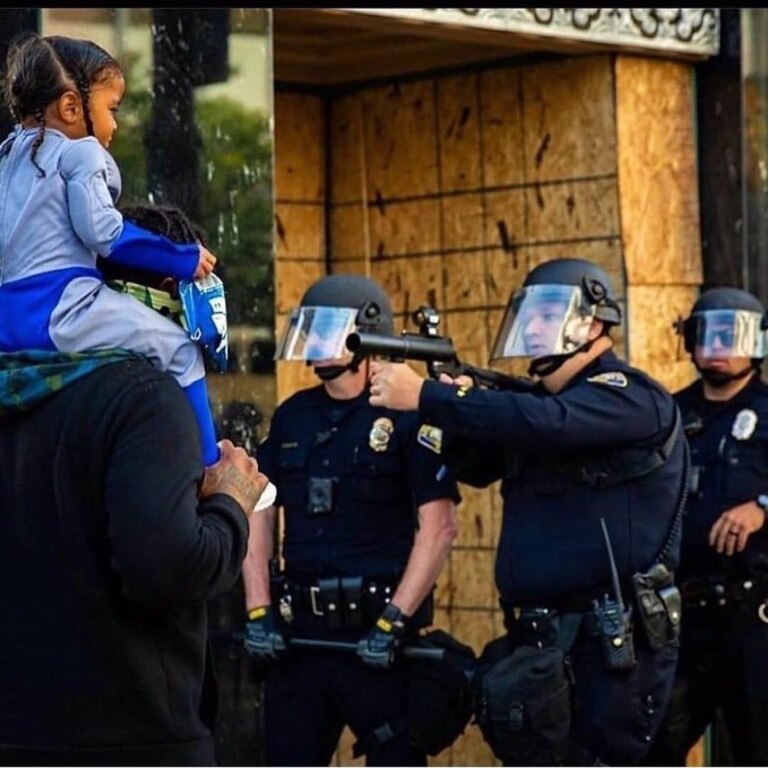 A protester with a child on his shoulders comes close to cops with rubber bullet guns. Picture: Richard Grant