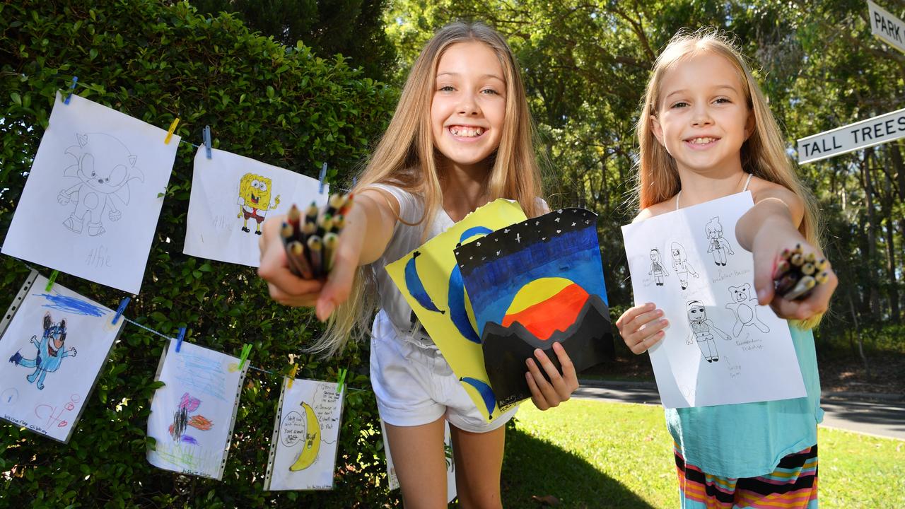 Avery and Deedee O'Mara of Caloundra add artwork to a hedge that encourages children to hang artwork, as a way to spread cheer through the community in isolation. Photo: John McCutcheon