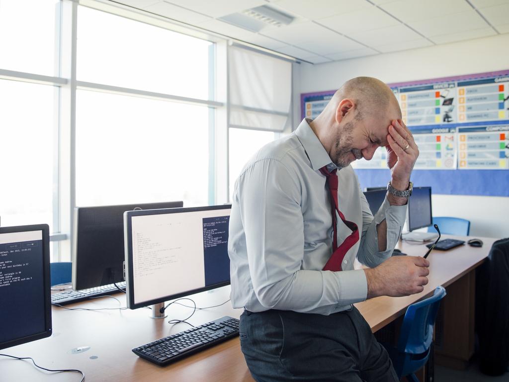 Stressed, concerned teacher sits on the edge of a desk in an empty classroom, schools, upset. Istock