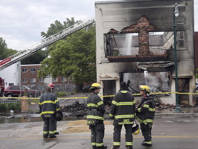 Firefighters stand as an aerial hose sends water on hot spots of a building destroyed in the riots. Picture: AP